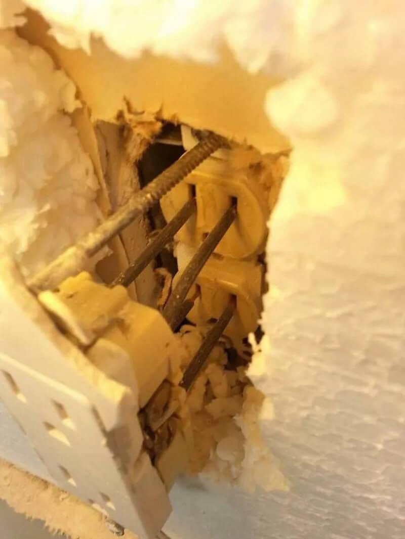 Close-up of an electrical outlet with exposed wiring and damaged wall.