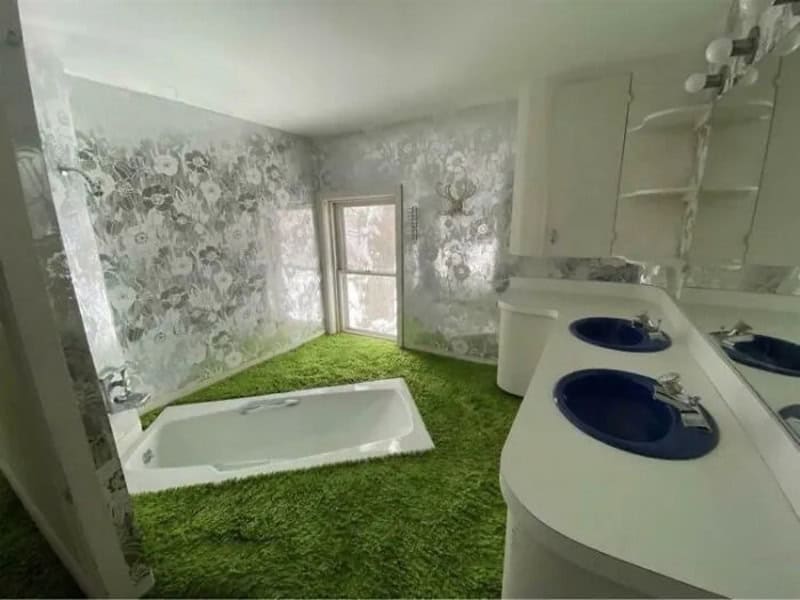 Bathroom with bathtub, green carpet, floral wallpaper, and double sinks.