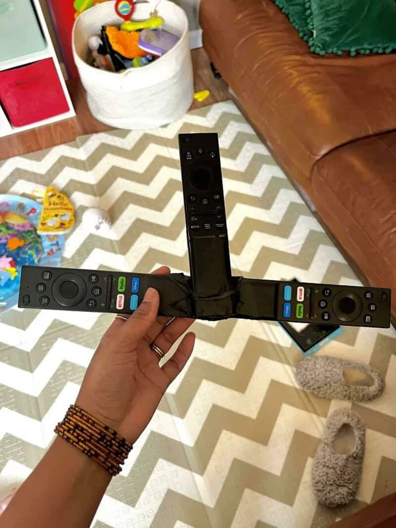 Person holding a broken TV remote control with tape, in a living room.