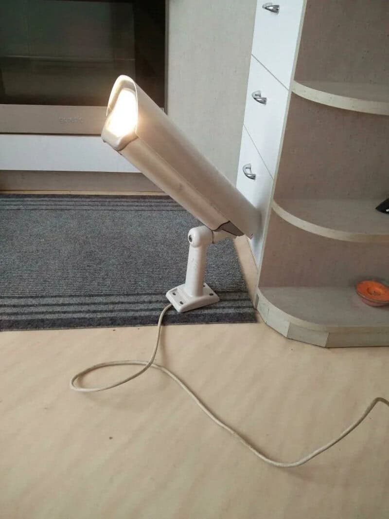 A makeshift lamp made from a cardboard tube and a light source, placed on the floor near a cabinet.