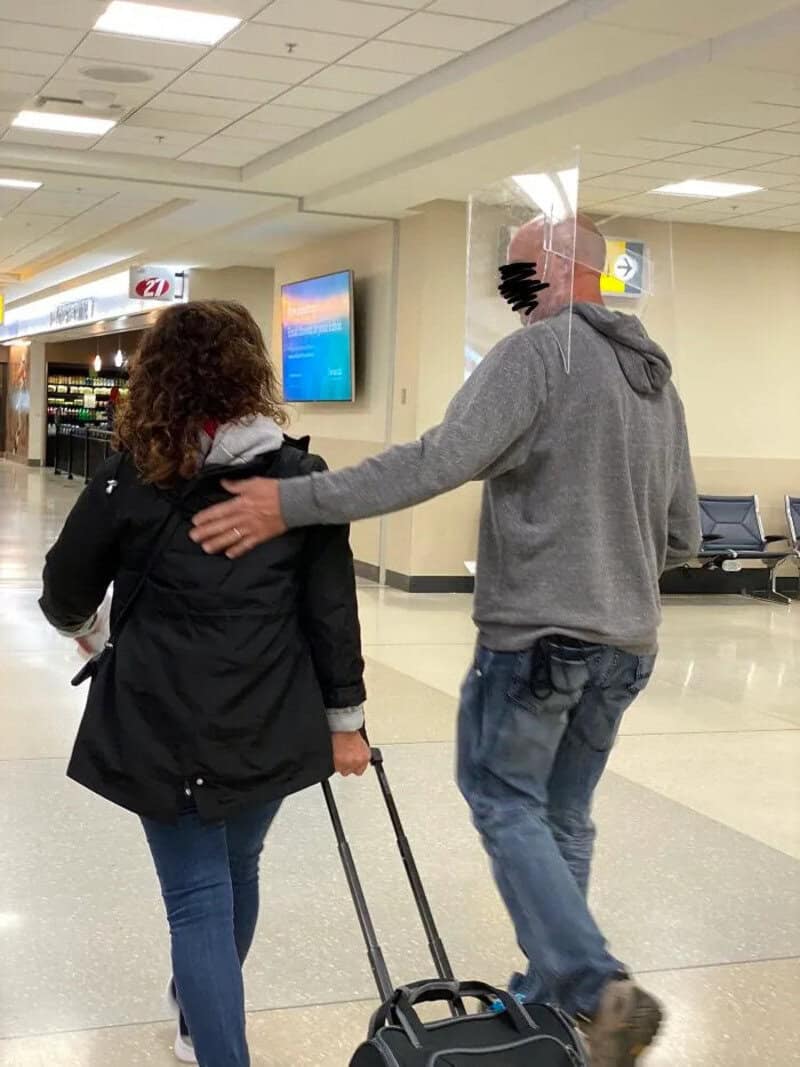 A man with a plastic bag over his head walking with a woman in an airport.