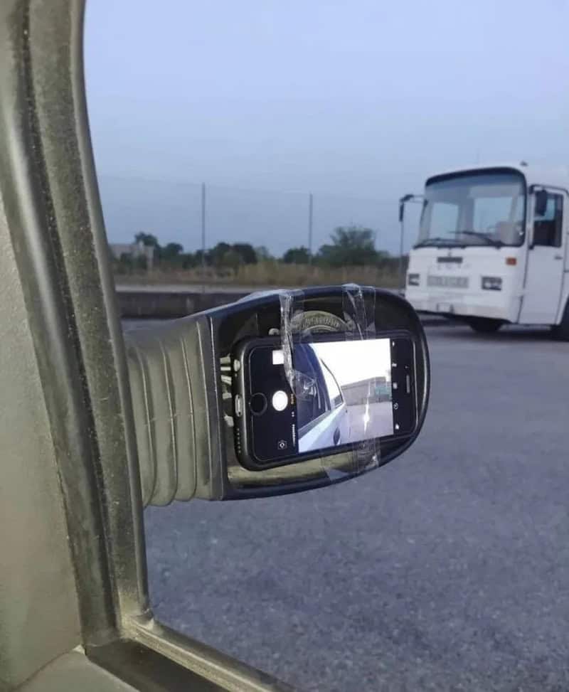 Cell phone stuck in a car's air vent, capturing a photo of a bus outside.