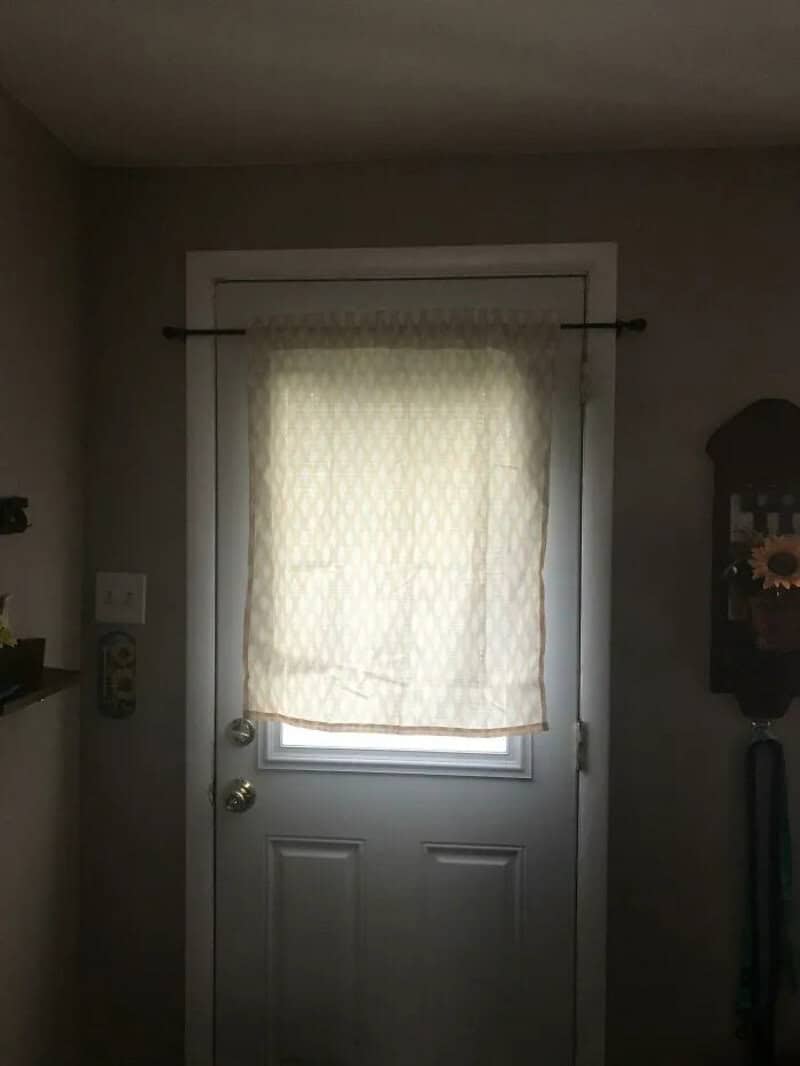 Door with a curtain, light coming through, in a room with gray walls.