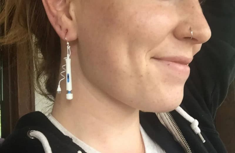 Close-up of a woman with a nose piercing and earrings, smiling slightly.