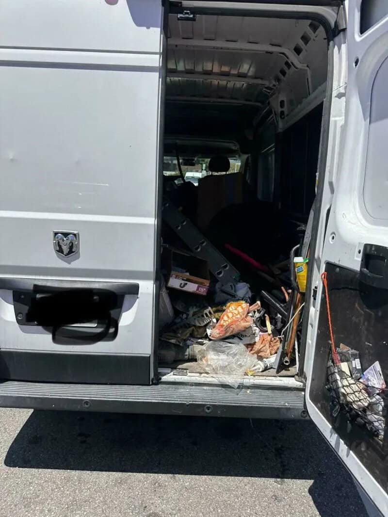 Cluttered van with tools and trash inside, parked on the street.