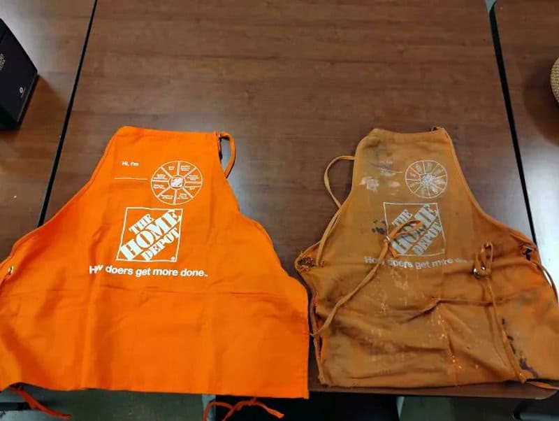 Two orange Home Depot aprons on a wooden table, one clean and one dirty.