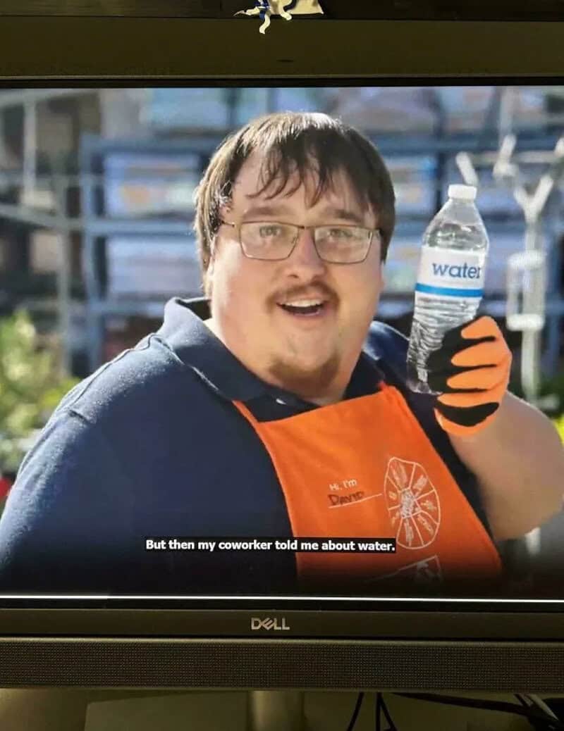 Man with glasses in orange apron holding water bottle, smiling.