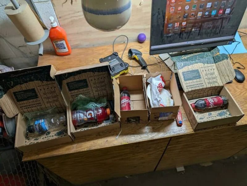 Disorganized desk with soda bottles, boxes, and office supplies.