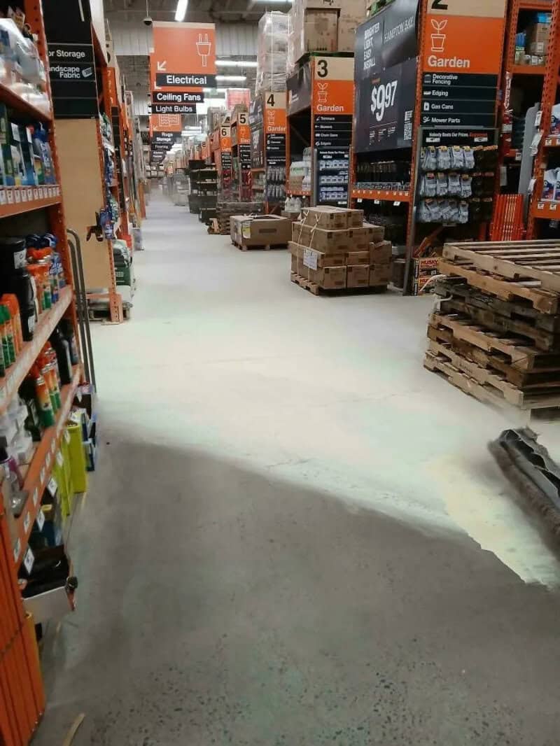 Aisle in Home Depot with shelves, boxes, and pallets, some areas with unfinished flooring.