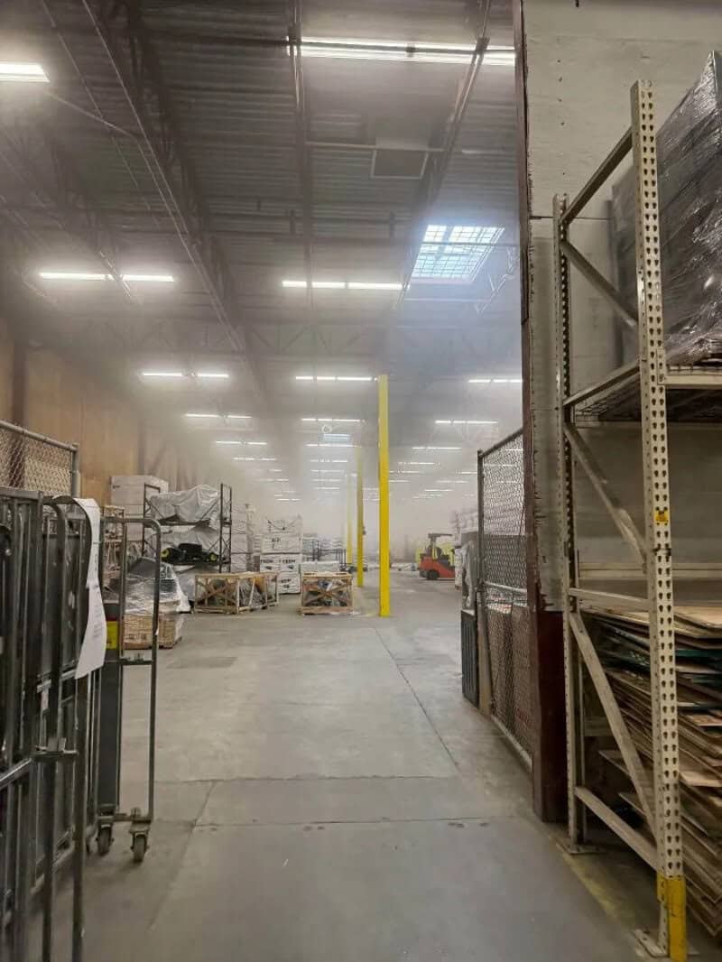 Warehouse aisle with shelves and carts, hazy atmosphere, bright overhead lights.