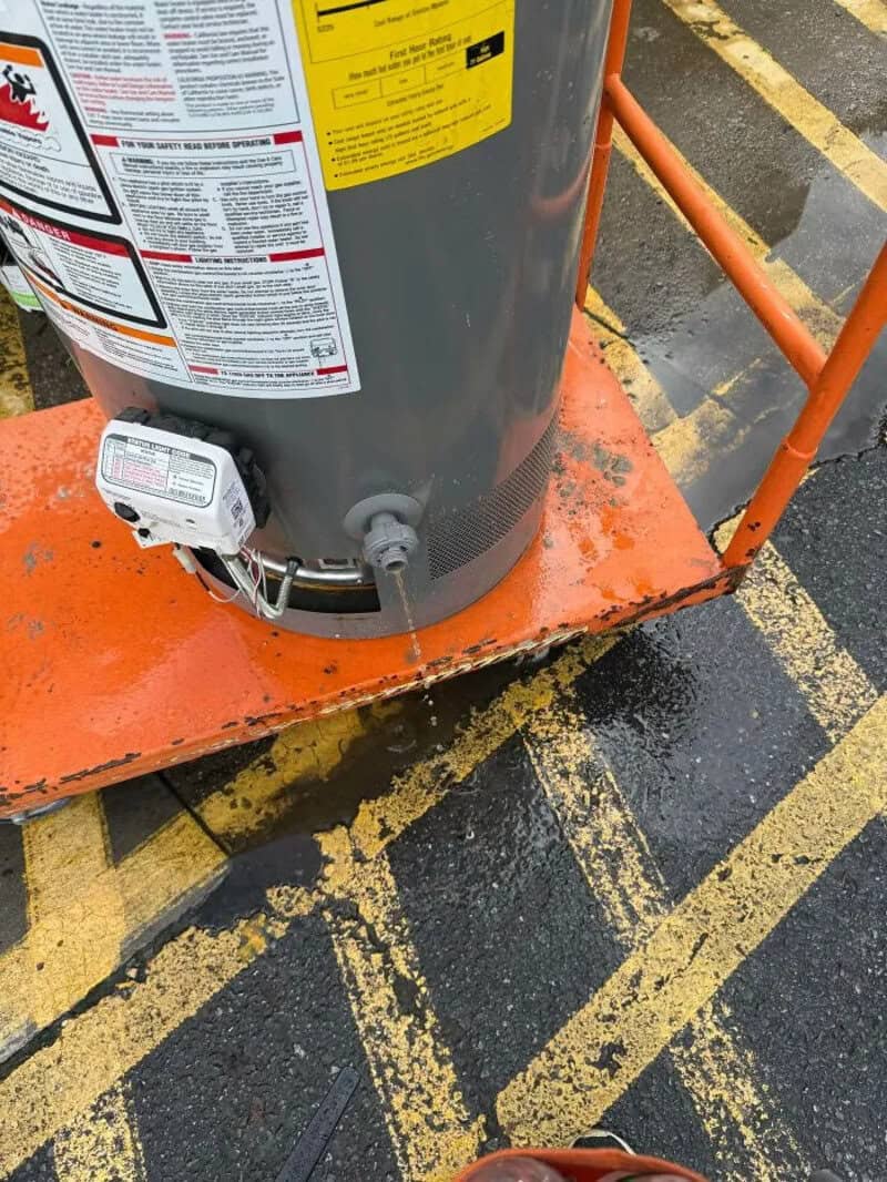 Gas water heater on orange cart with warning labels and a control device.