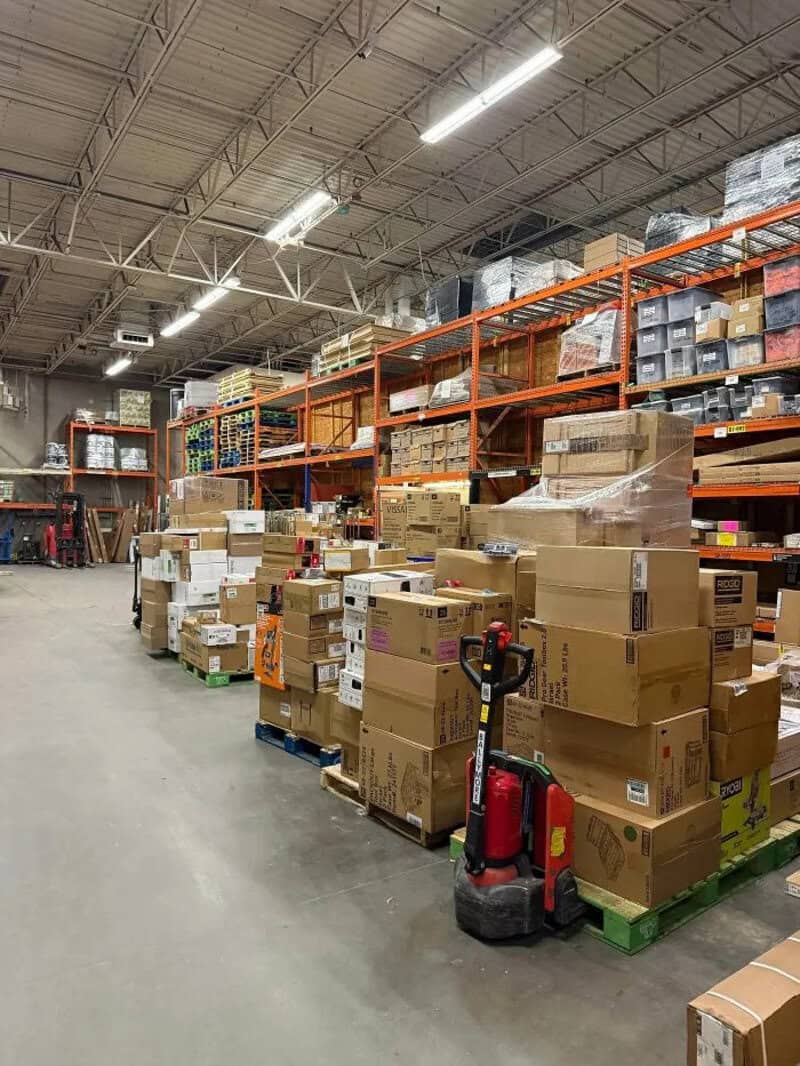 Warehouse aisle with stacked boxes and a pallet jack in the foreground.