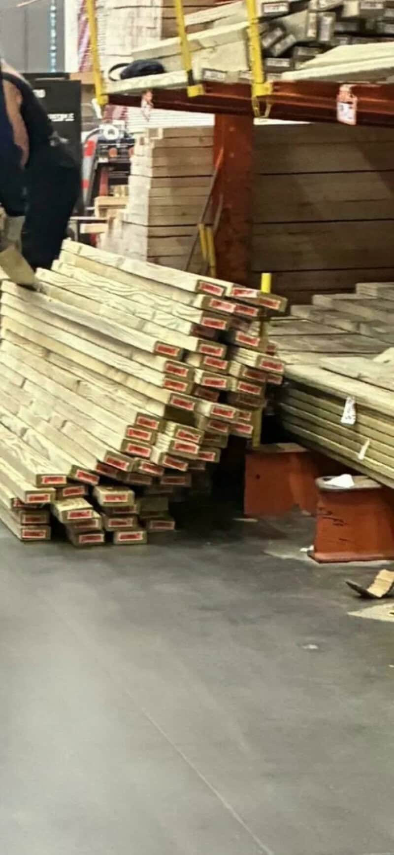 Stack of wood planks in a hardware store aisle with a person partially visible.