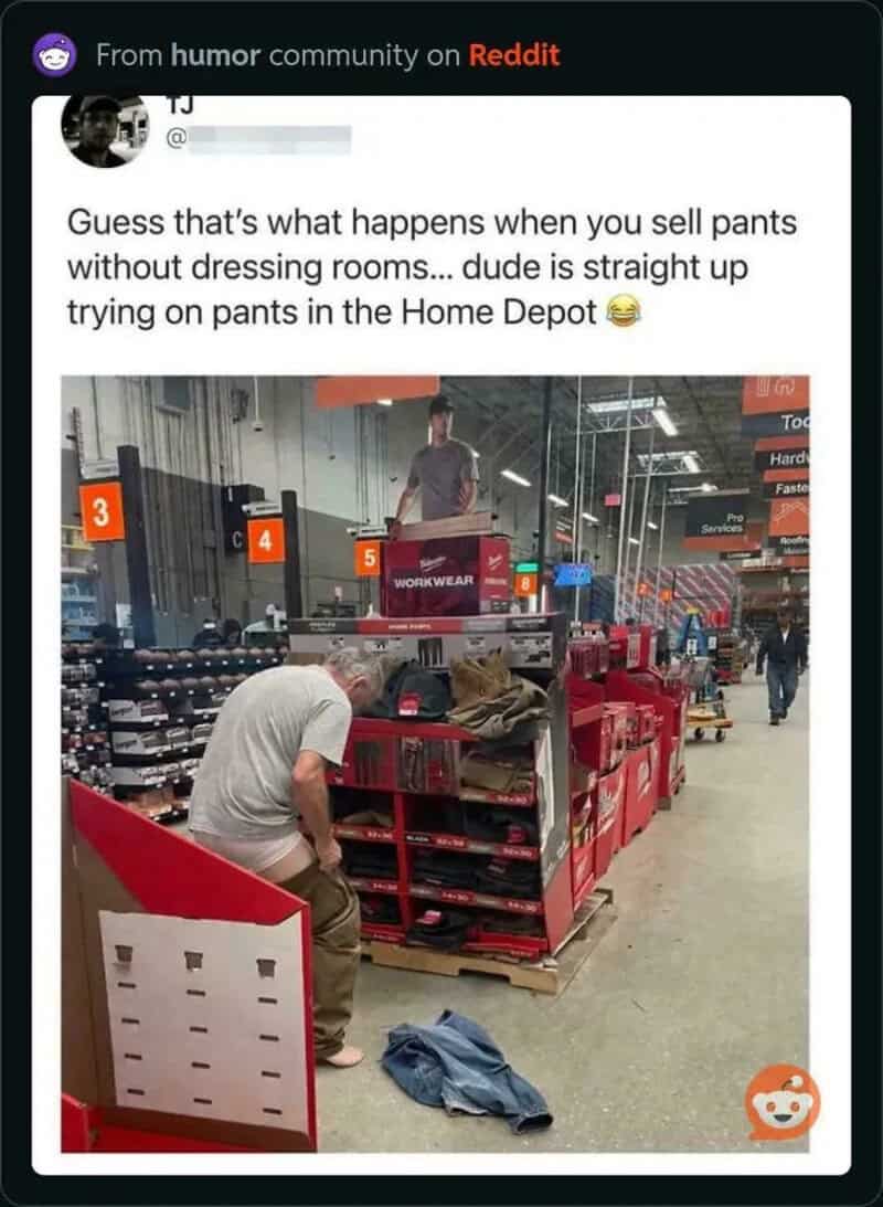 Man sitting on a red cart in Home Depot without dressing room, trying on pants.