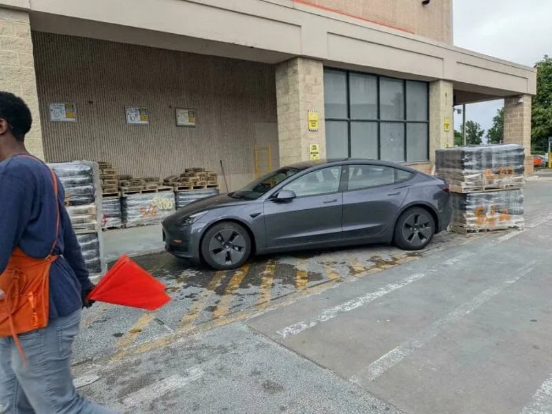 Tesla Model 3 parked in a handicapped space outside a store.