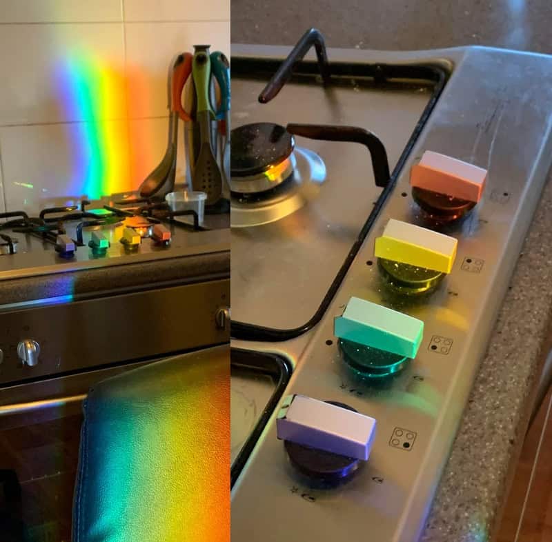 Rainbow light on stove with colorful teapots and kitchen utensils.