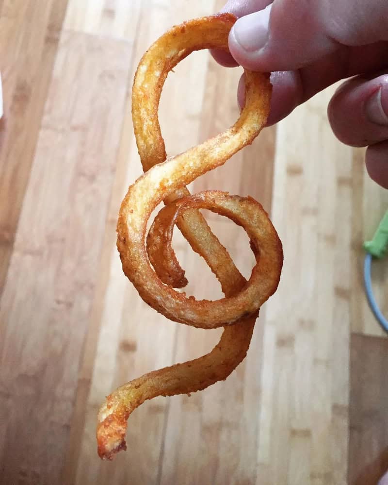 Fried onion ring shaped like a spiral, held by a person's hand.