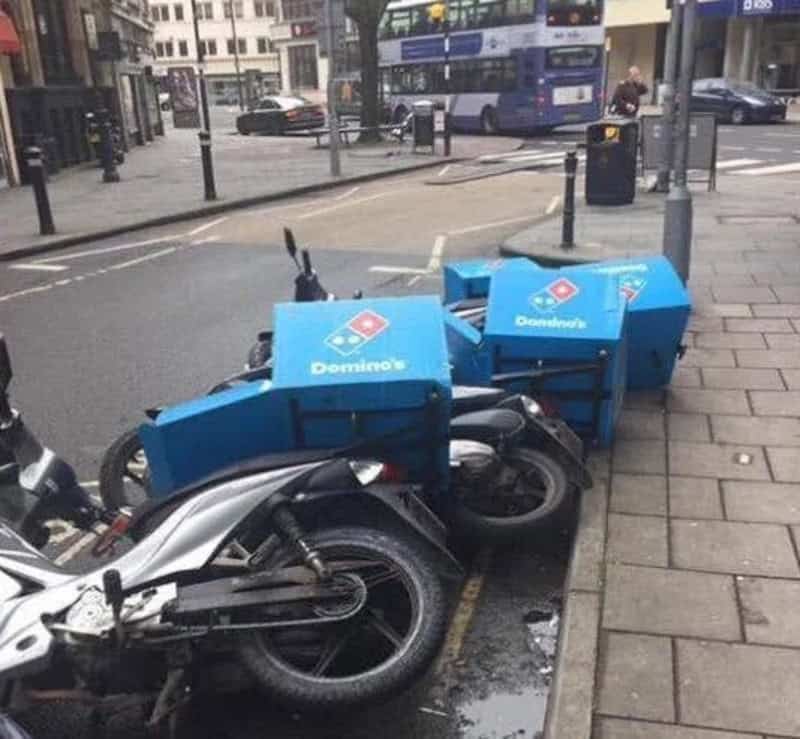 Two Domino's pizza delivery bikes parked on the sidewalk with blue boxes.