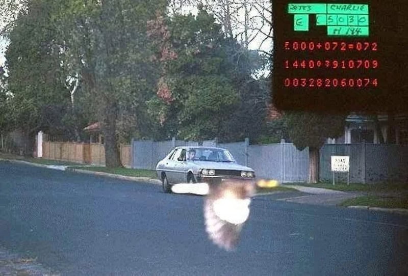 A car on a suburban street with a large, blurry, white object in front of it.