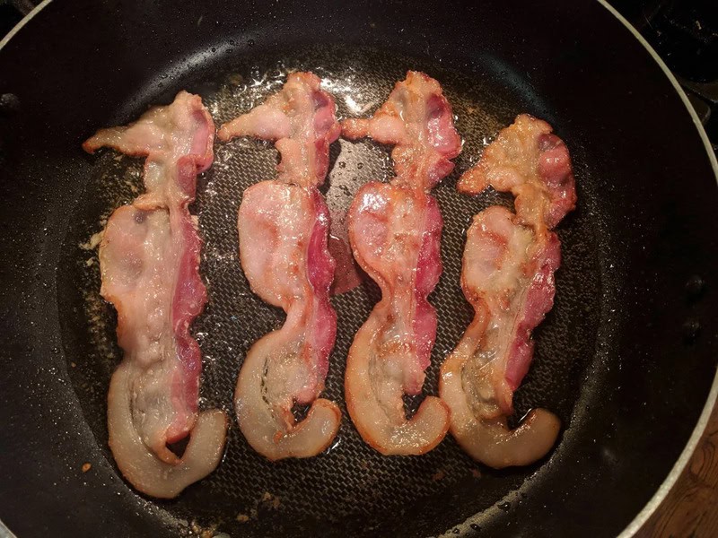 Bacon strips shaped like the number 8 in a frying pan.