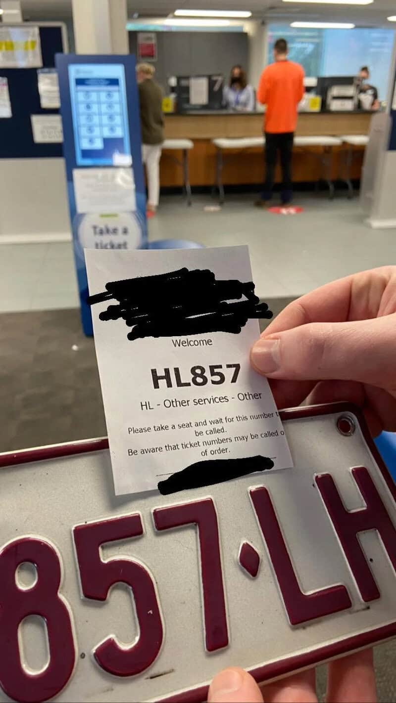 Person holding a ticket and a license plate at a service counter.