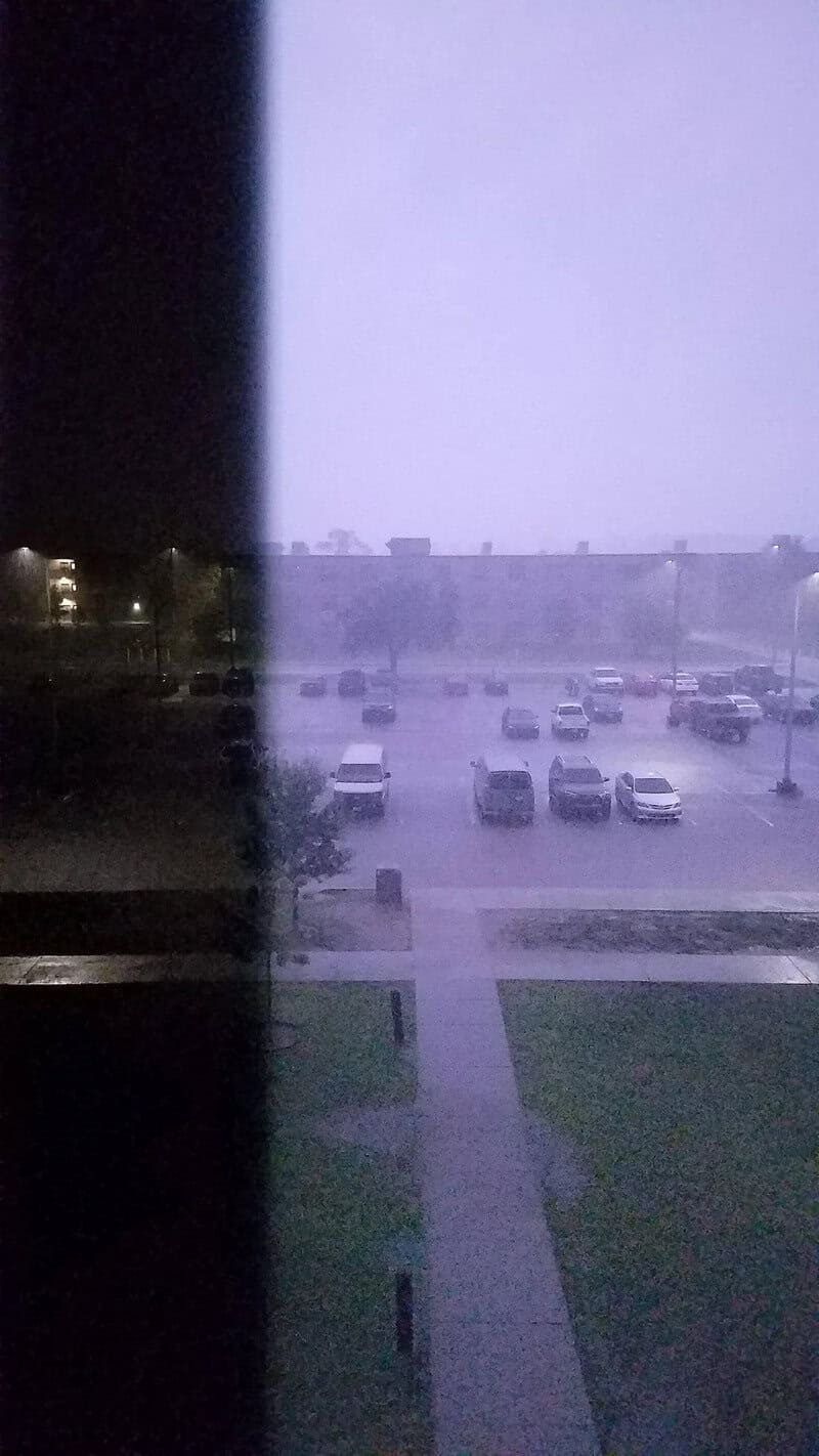 View of a parking lot during a storm with heavy rain and lightning.