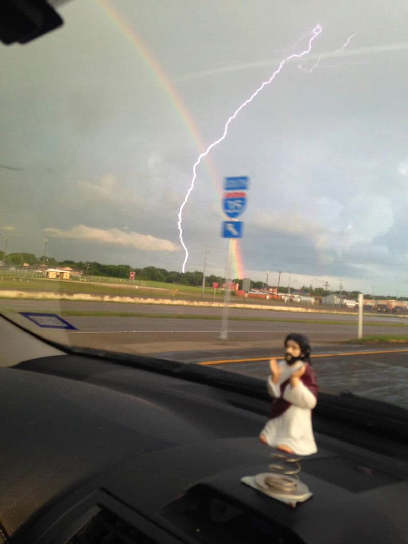 Lightning strikes near a rainbow over a highway with a child in a white dress in the foreground.
