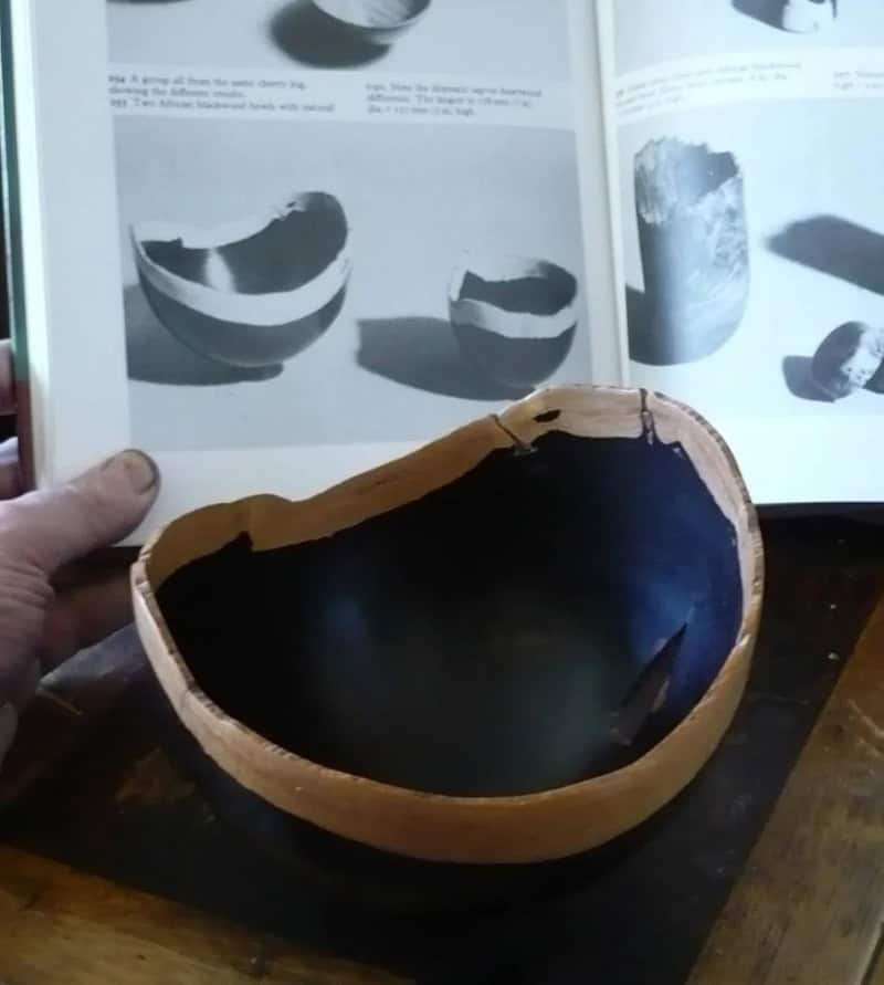 Broken bowl with black interior and a book with images of bowls in the background.