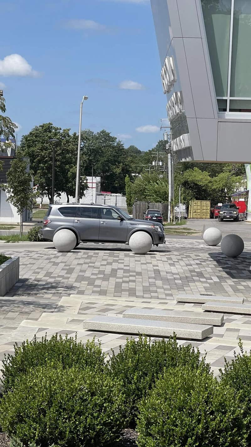 A grey car parked near large white spherical bollards outside a modern building.