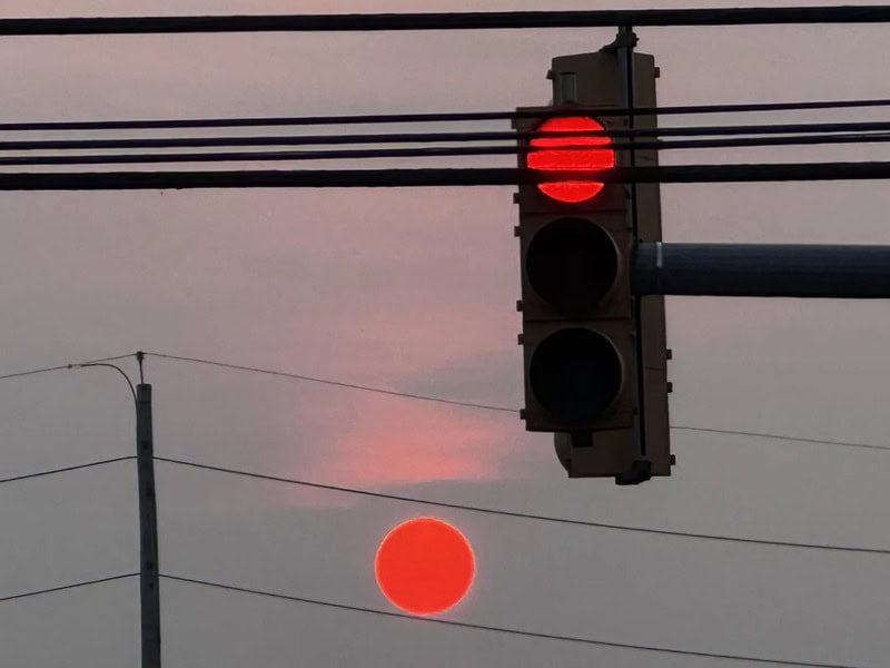 Red traffic light and a red sun aligned in the sky.