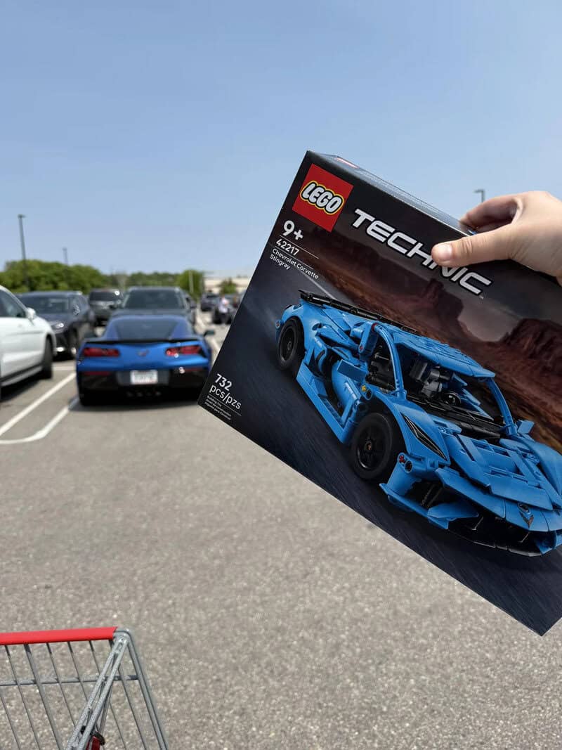 Person holding LEGO Technic Lamborghini box in parking lot with cars.