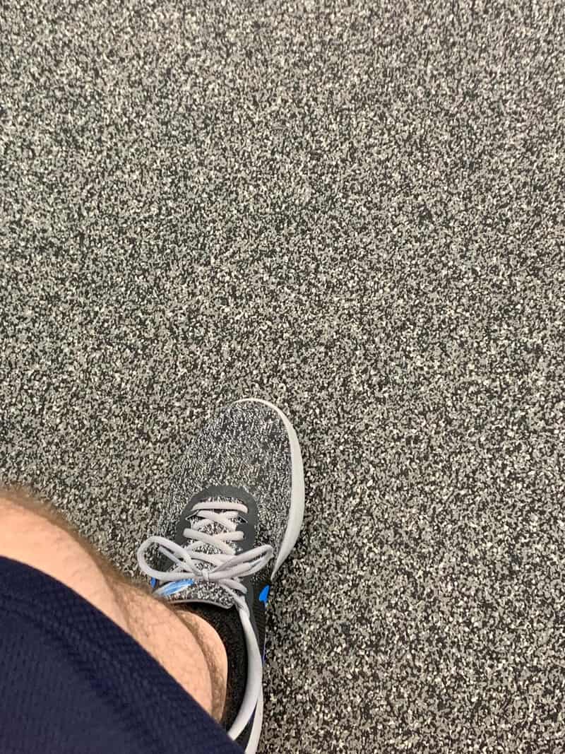A person's foot in a sneaker on a textured ground, with a white curved line nearby.