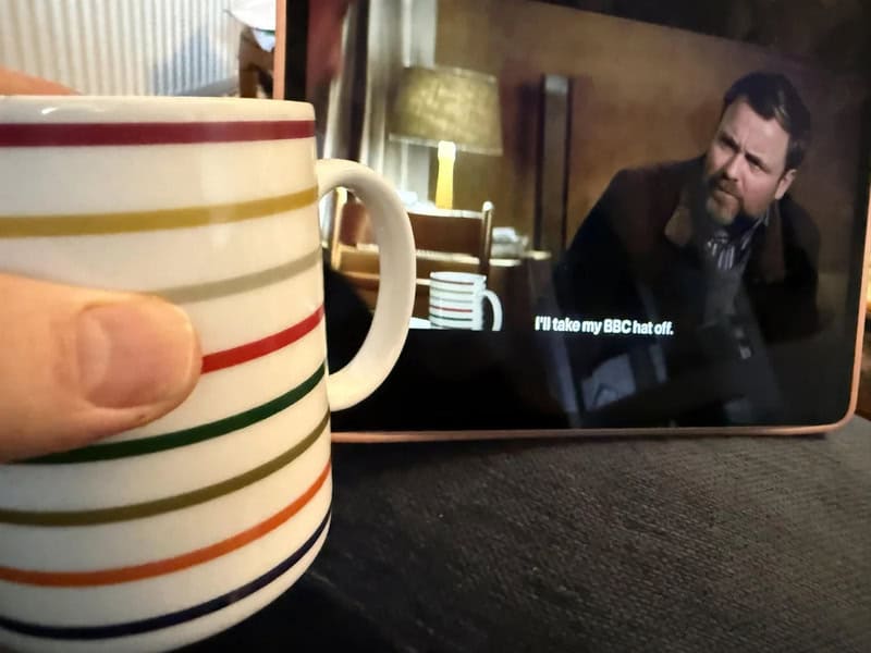 A hand holding a striped mug in front of a tablet showing a man with a beard.