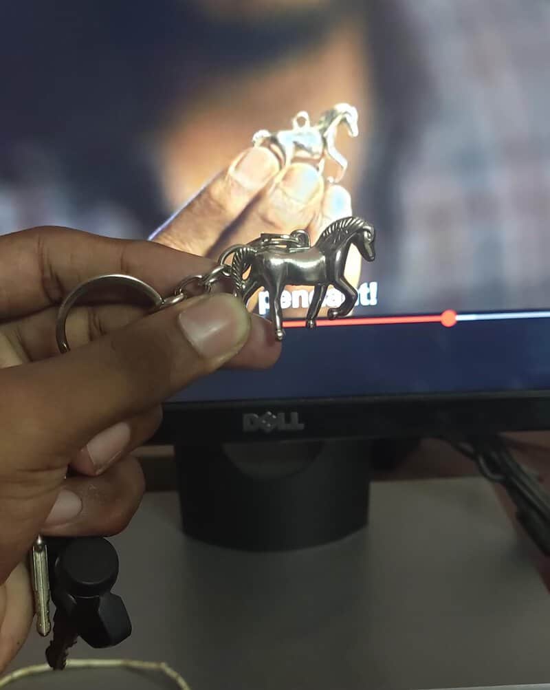 Hand holding a keychain with a horse-shaped charm in front of a computer screen.