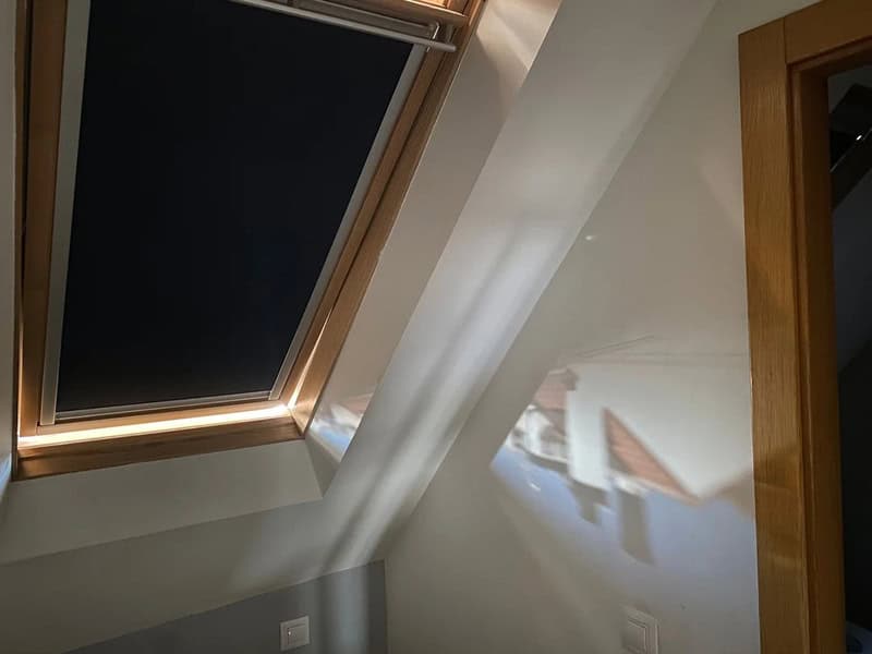 Sunlight streaming through a skylight onto a white wall and a wooden door frame.