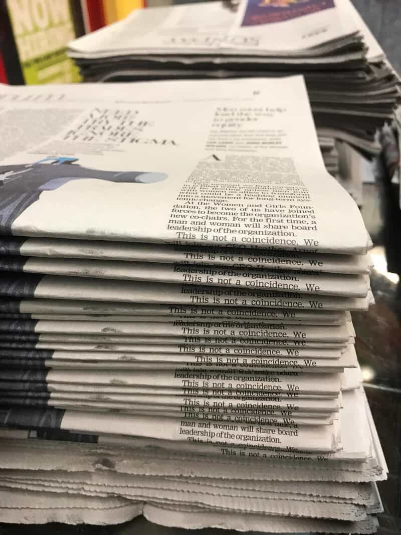 Stack of newspapers with a headline about coincidences and a person in a suit on the front page.