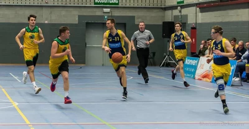Basketball players in yellow and blue jerseys running on indoor court.