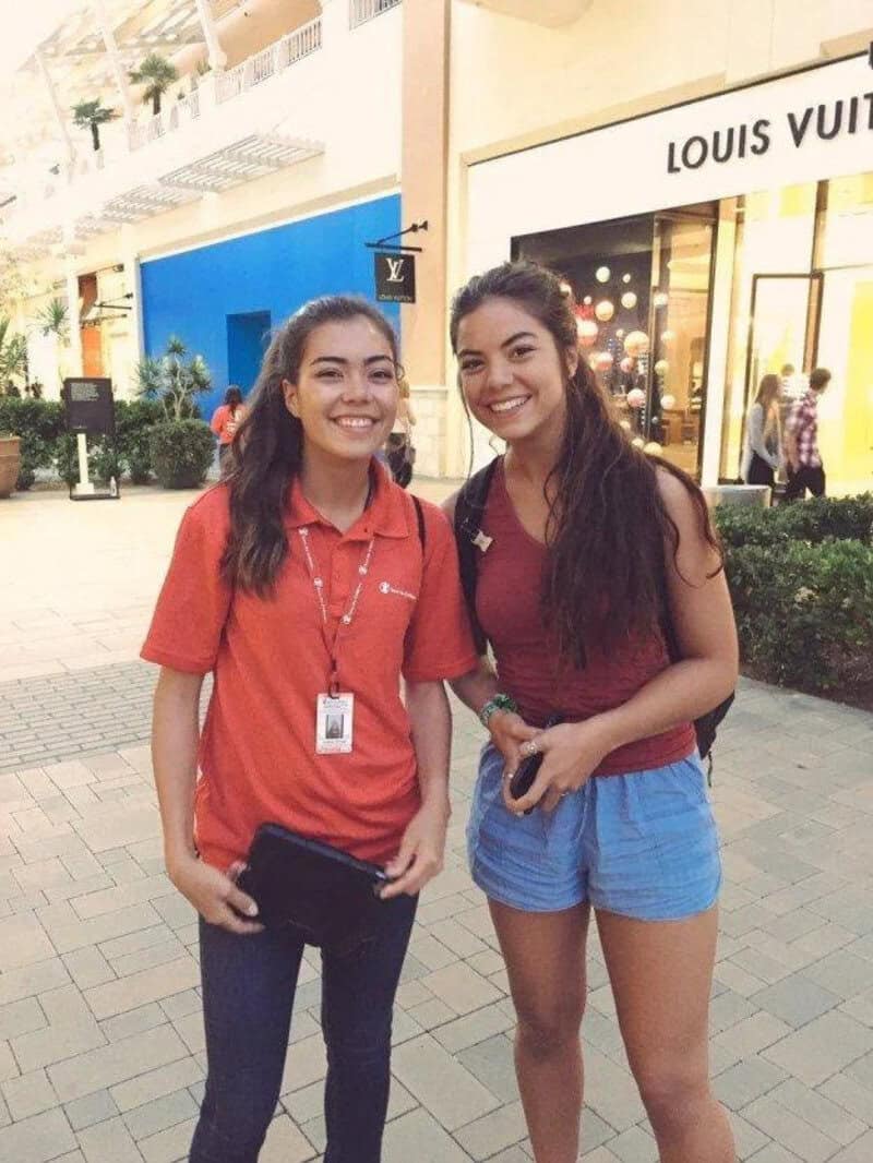 Two young women smiling outside Louis Vuitton store in a shopping mall.