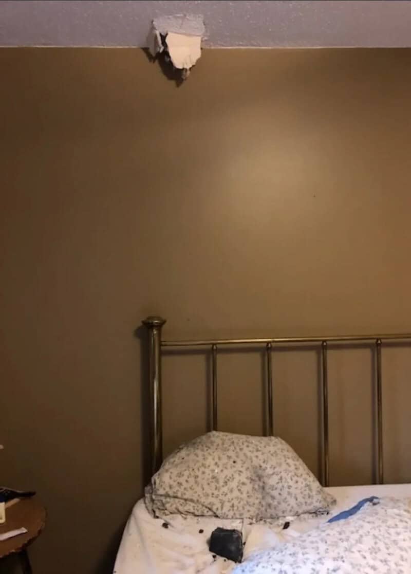 Ceiling hole above bed with pillow and phone on bed.