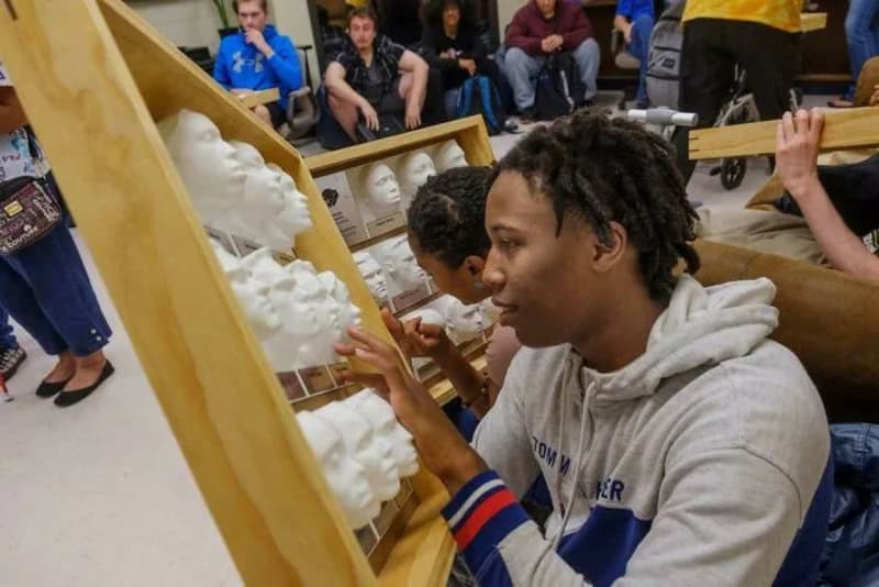 Young man touching 3D printed skulls at a workshop event.
