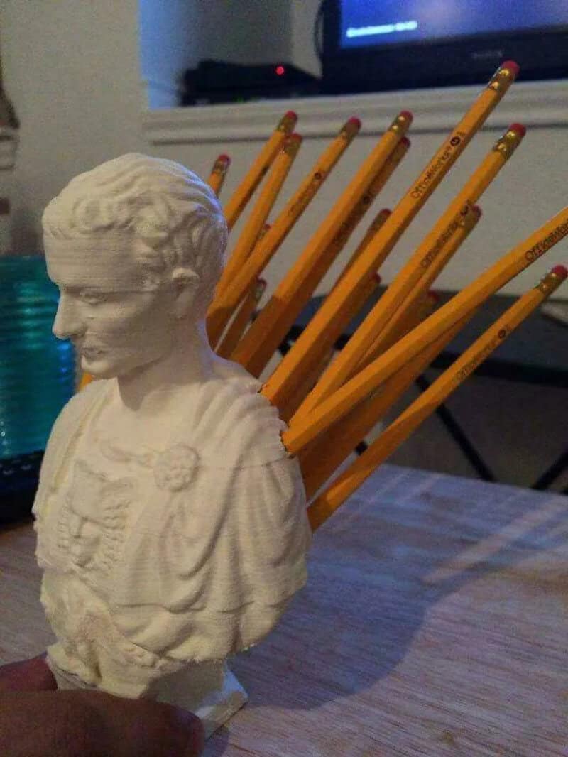 Bust of a man with pencils in his back, on a wooden table.