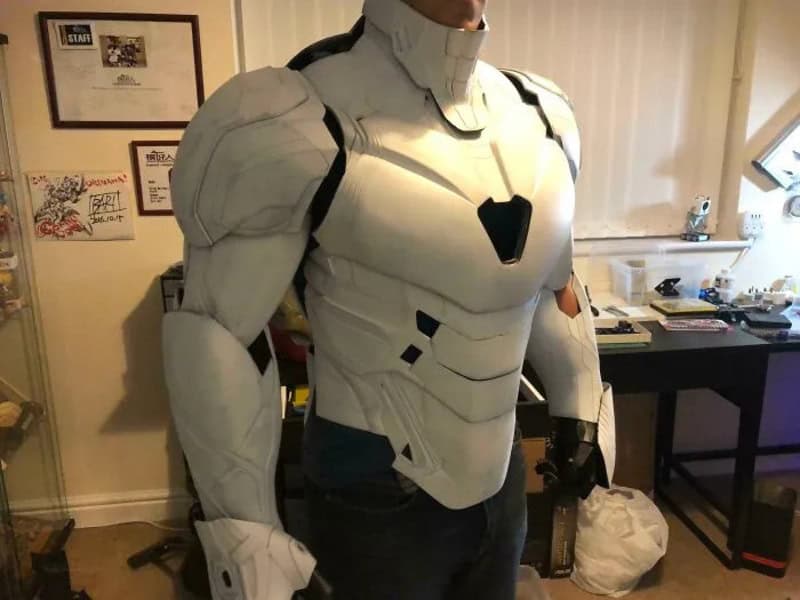 Person in a white futuristic armor suit in a room with framed pictures and a desk.
