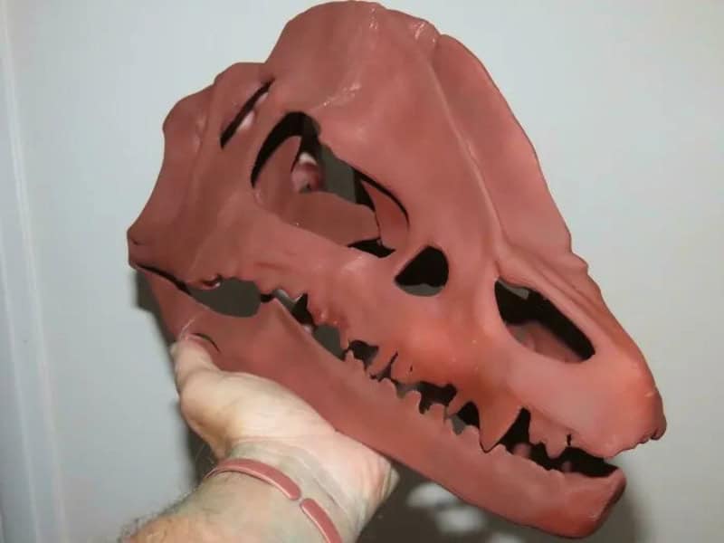 3D printed dinosaur skull model in pink with black details, held by a hand.