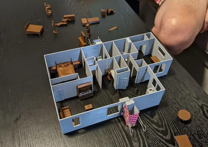 3D printed dollhouse with furniture and small accessories on a black table.