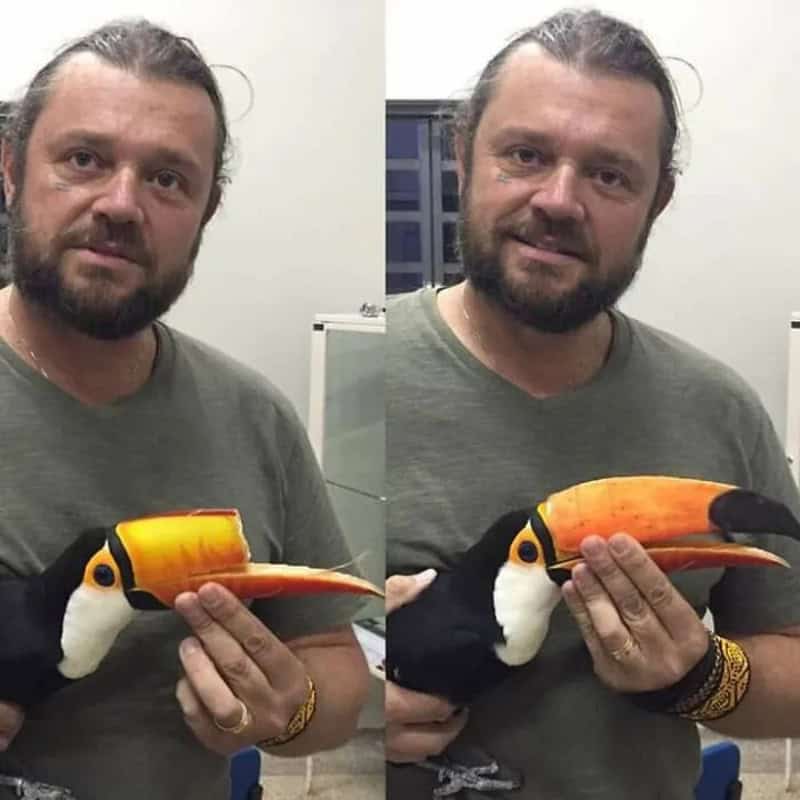Man holding a 3D-printed toucan model in front of a mirror.