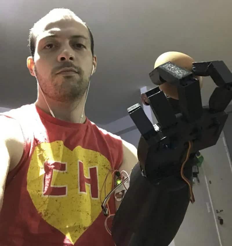 Man in red shirt holding a robotic hand with a yellow ball on top.