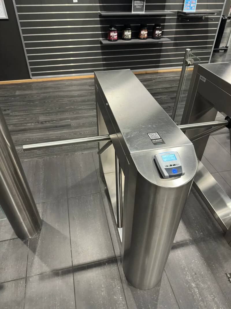 Metal turnstile gate in a modern indoor setting with black wall and wooden floor.