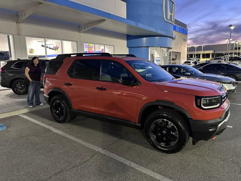 Red SUV parked outside Honda dealership with person standing nearby.