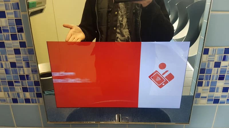 Person taking a mirror selfie in a bathroom with a red and white sign.