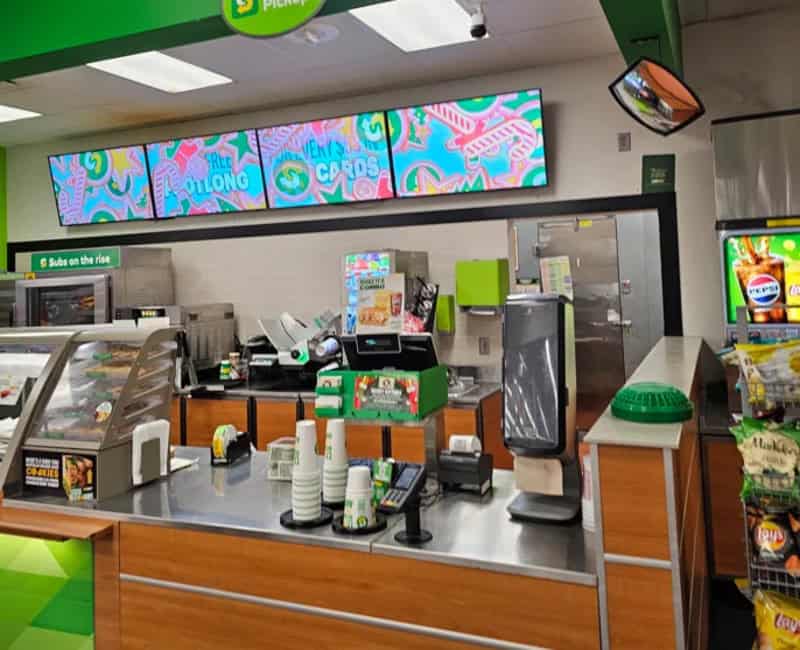Grocery store checkout counter with digital screens and various items.